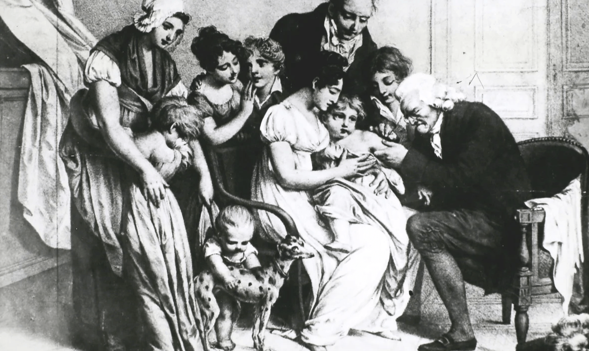 An 18th-century engraving depicting Dr. Edward Jenner performing the first smallpox vaccination on a young child, surrounded by a group of onlookers in a domestic setting.